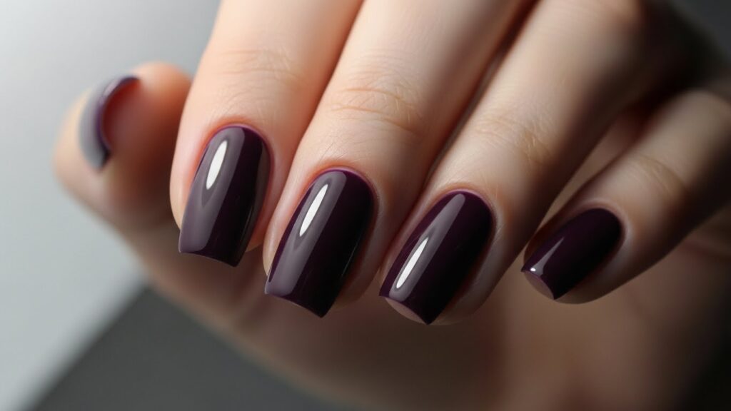Dark plum purple winter nails, glossy finish, soft studio lighting.