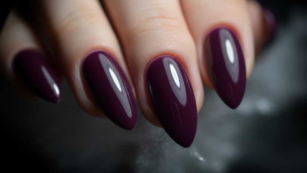 Deep plum purple winter nails in almond shape with moody soft winter lighting.